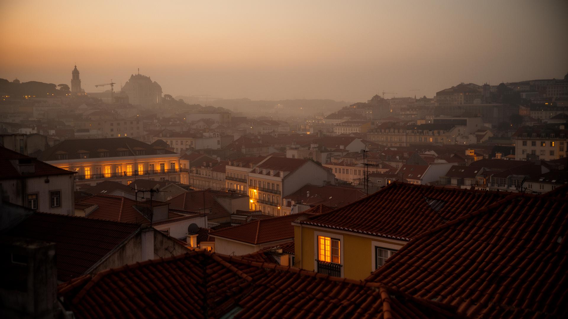 Lisbon rooftops at dusk with warm window lights glowing across the city.